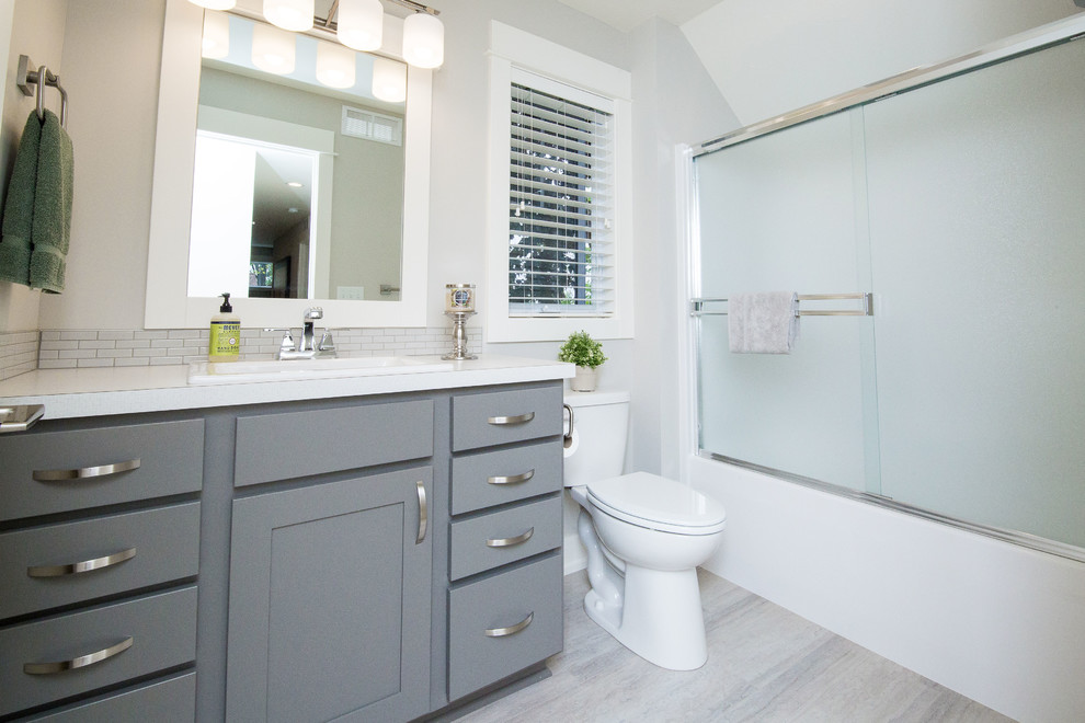 Réalisation d'une salle d'eau tradition de taille moyenne avec un placard à porte shaker, des portes de placard bleues, une baignoire en alcôve, un combiné douche/baignoire, WC séparés, un carrelage blanc, des carreaux de céramique, un mur gris, un sol en vinyl, un lavabo posé, un plan de toilette en stratifié, un sol gris, une cabine de douche à porte coulissante et un plan de toilette blanc.