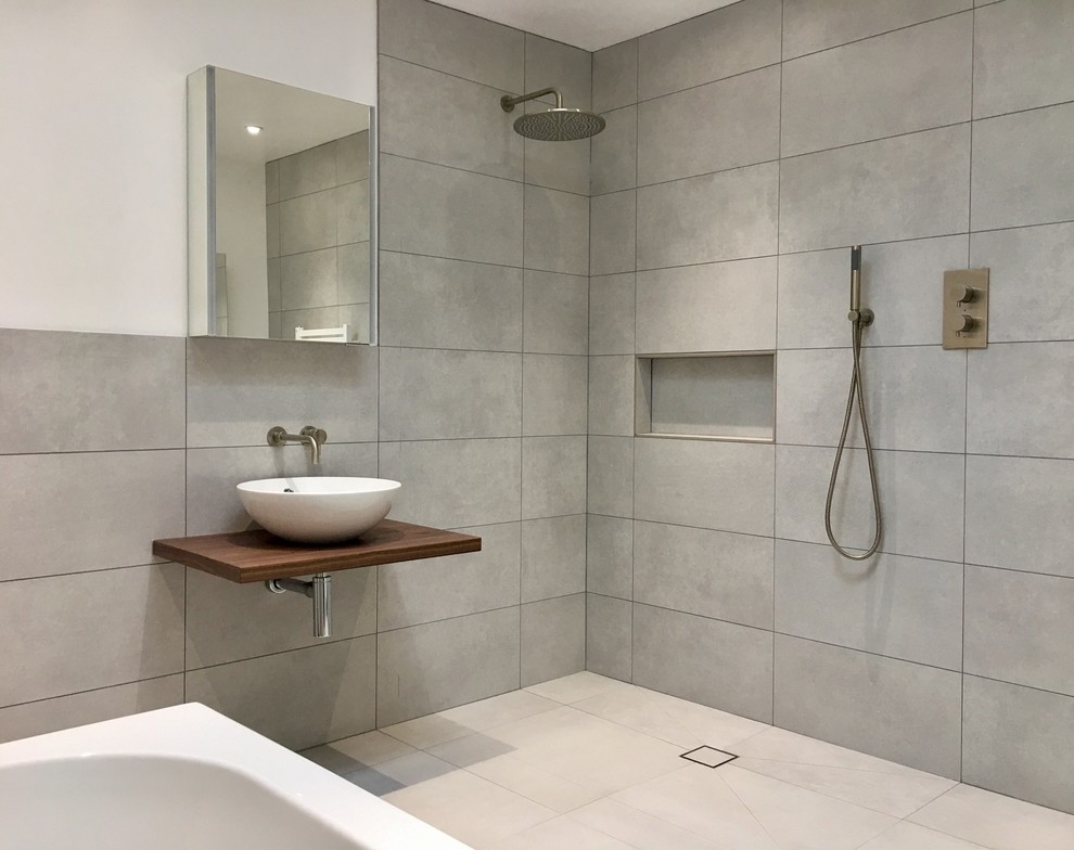 Idéer för mellanstora funkis en-suite badrum, med släta luckor, ett platsbyggt badkar, våtrum, en vägghängd toalettstol, grå kakel, porslinskakel, grå väggar, klinkergolv i porslin, ett fristående handfat, träbänkskiva och grått golv