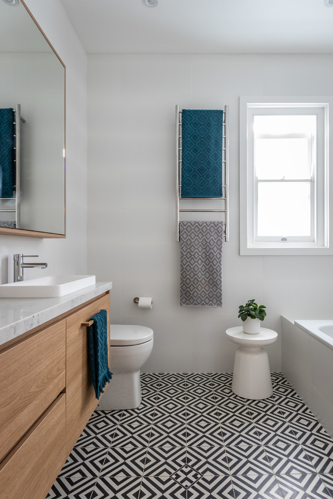Inredning av ett modernt flerfärgad flerfärgat badrum med dusch, med ett badkar i en alkov, vita väggar, ett nedsänkt handfat, flerfärgat golv, skåp i ljust trä, en vägghängd toalettstol, vit kakel, keramikplattor, klinkergolv i keramik, marmorbänkskiva och släta luckor
