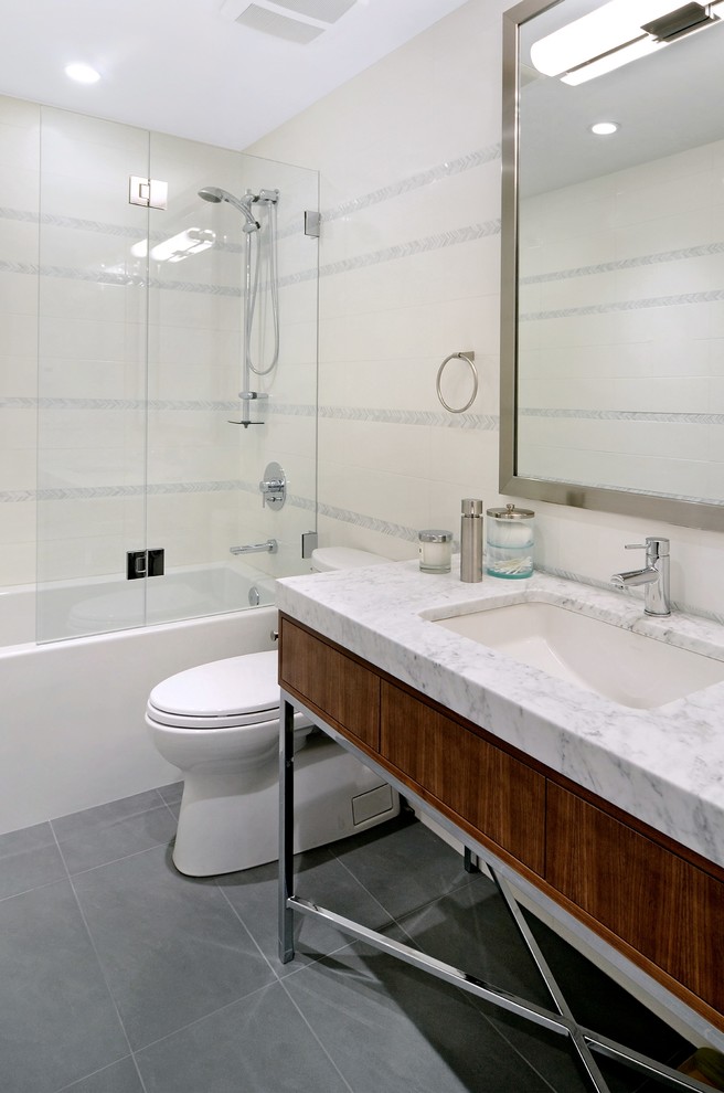 Cette photo montre une salle de bain tendance en bois brun avec un placard à porte plane, un combiné douche/baignoire, un carrelage blanc, un carrelage métro, un mur jaune, un sol en carrelage de porcelaine, un lavabo encastré et un plan de toilette en marbre.