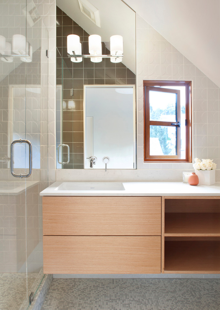 Пример оригинального дизайна: маленькая ванная комната в стиле модернизм с плоскими фасадами, светлыми деревянными фасадами, полом из мозаичной плитки, душевой кабиной, столешницей из искусственного кварца, стеклянной плиткой, душем в нише, врезной раковиной, белыми стенами и серой плиткой для на участке и в саду