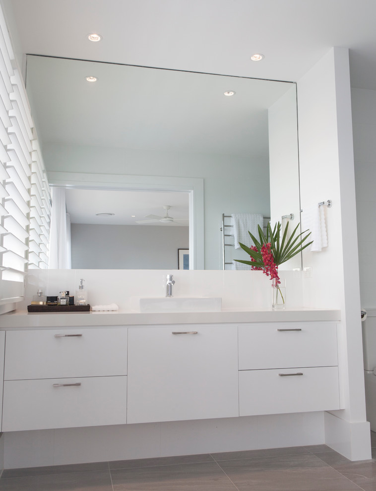 Example of a mid-sized beach style master gray tile and porcelain tile porcelain tile doorless shower design in Sydney with a vessel sink, flat-panel cabinets, white cabinets, quartz countertops, a one-piece toilet and white walls