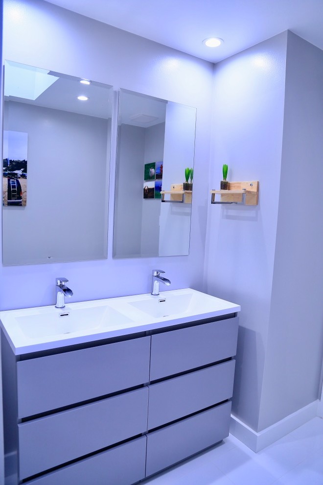 Photo of a medium sized contemporary family bathroom in Houston with flat-panel cabinets, grey cabinets, an alcove shower, a two-piece toilet, grey tiles, pebble tiles, grey walls, porcelain flooring, an integrated sink, solid surface worktops, white floors, a sliding door and white worktops.