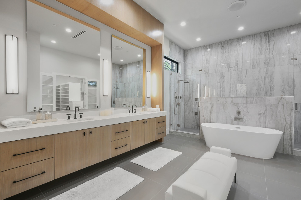 Inspiration for a large contemporary ensuite bathroom in Dallas with flat-panel cabinets, light wood cabinets, a freestanding bath, a double shower, grey tiles, porcelain tiles, white walls, porcelain flooring, a submerged sink, engineered stone worktops, grey floors, a hinged door, white worktops, double sinks and a built in vanity unit.