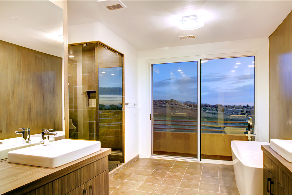 Exempel på ett mellanstort modernt en-suite badrum, med släta luckor, skåp i mellenmörkt trä, en toalettstol med separat cisternkåpa, vit kakel, porslinskakel, grå väggar, ett fristående handfat, träbänkskiva, ett fristående badkar, en hörndusch och travertin golv