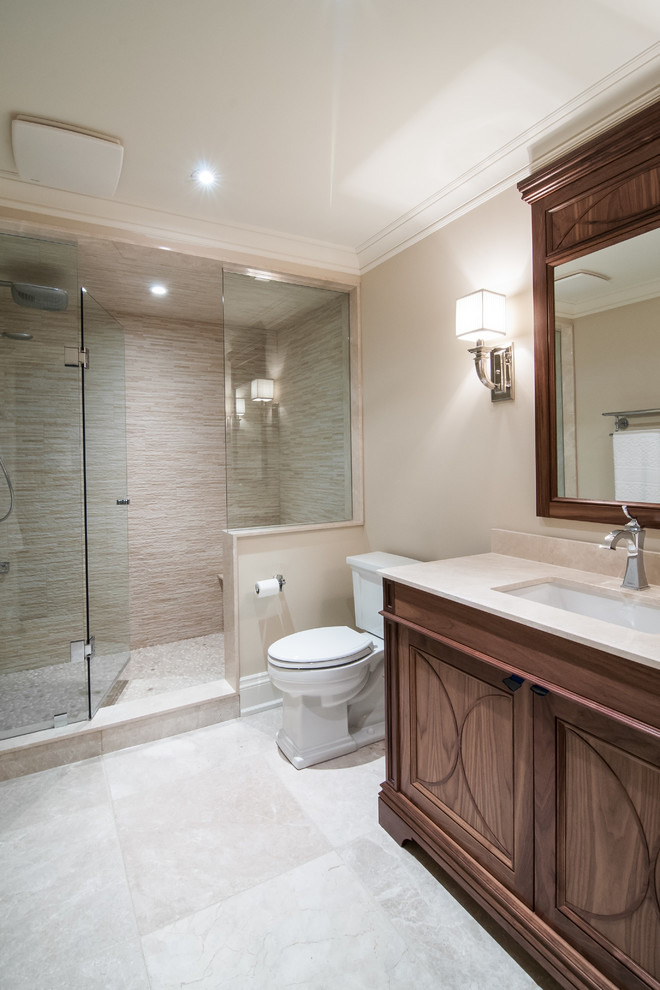 Пример оригинального дизайна: большая ванная комната в классическом стиле с фасадами с утопленной филенкой, фасадами цвета дерева среднего тона, душем в нише, унитазом-моноблоком, бежевой плиткой, галечной плиткой, бежевыми стенами, полом из известняка, душевой кабиной, врезной раковиной и мраморной столешницей