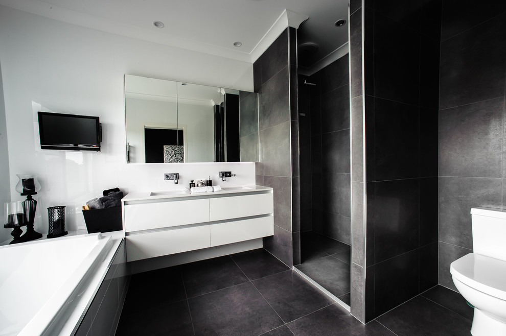 На фото: главная ванная комната в современном стиле с плоскими фасадами, белыми фасадами, ванной в нише, угловым душем, раздельным унитазом, черной плиткой, серыми стенами, врезной раковиной, черным полом, открытым душем и белой столешницей с