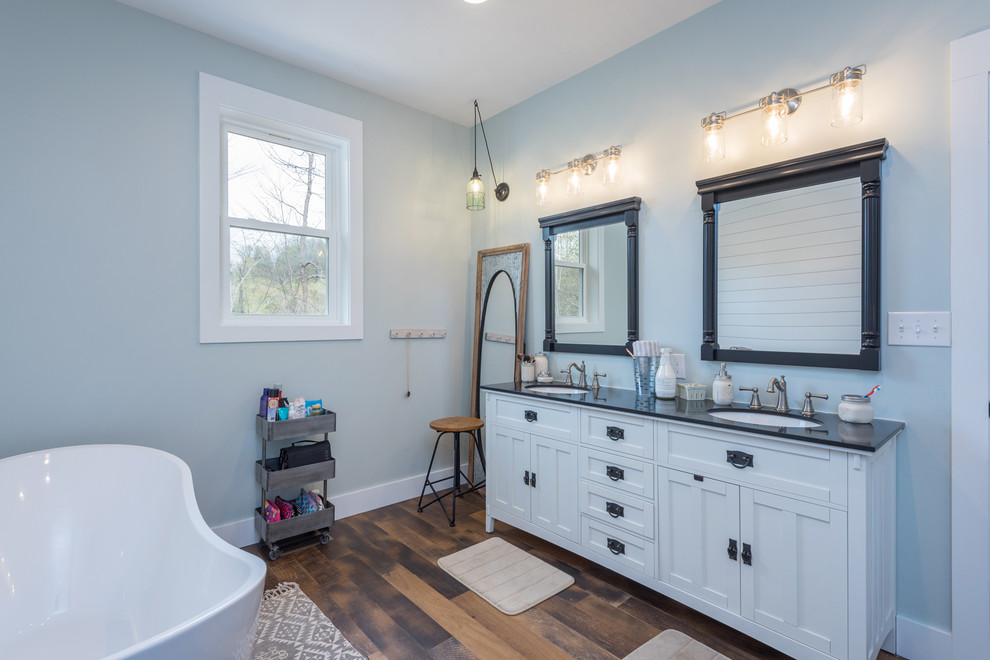 Medium sized traditional ensuite bathroom in Other with shaker cabinets, white cabinets, a freestanding bath, blue tiles, medium hardwood flooring, granite worktops, brown floors and black worktops.