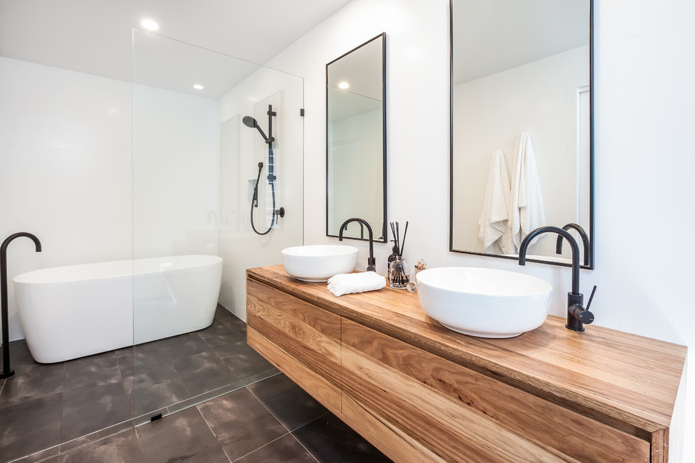 Cette photo montre une salle d'eau moderne en bois clair avec une baignoire indépendante, un combiné douche/baignoire, un carrelage blanc, carreaux de ciment au sol, un plan de toilette en bois, un sol gris et aucune cabine.