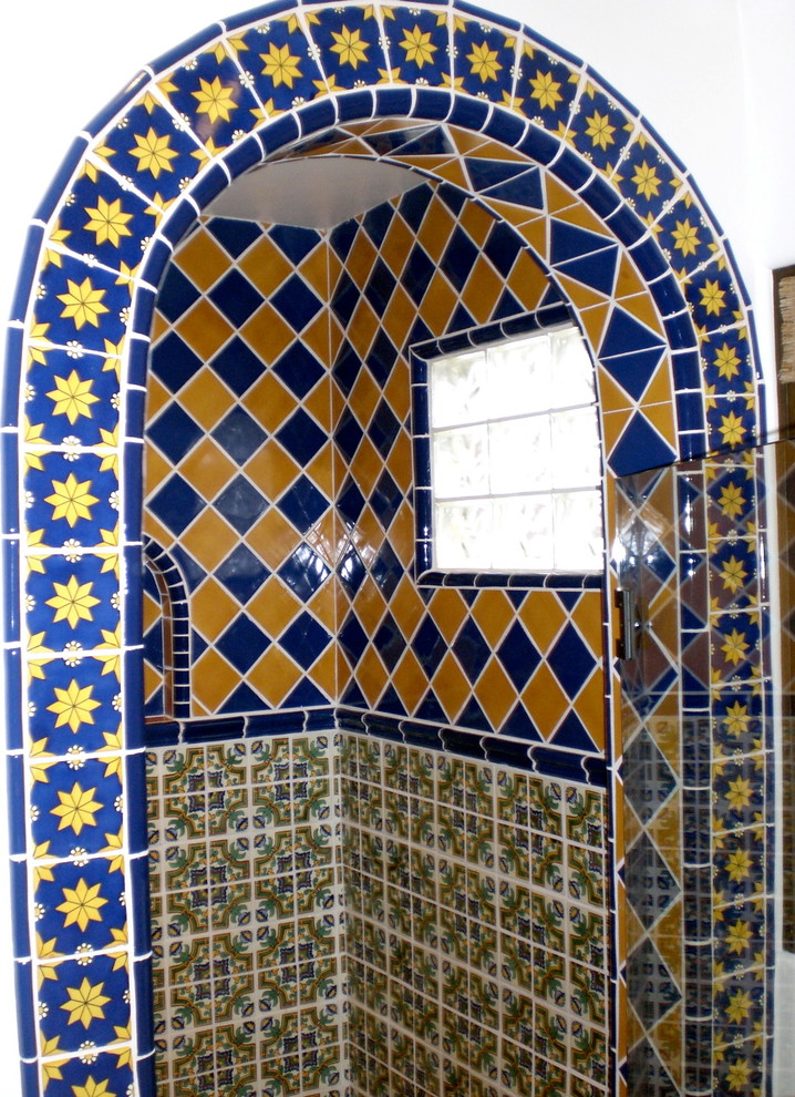 Photo of a medium sized mediterranean ensuite bathroom with raised-panel cabinets, medium wood cabinets, tiled worktops, ceramic tiles, a corner bath, a walk-in shower, a one-piece toilet, a built-in sink, white walls, blue tiles, yellow tiles and terracotta flooring.