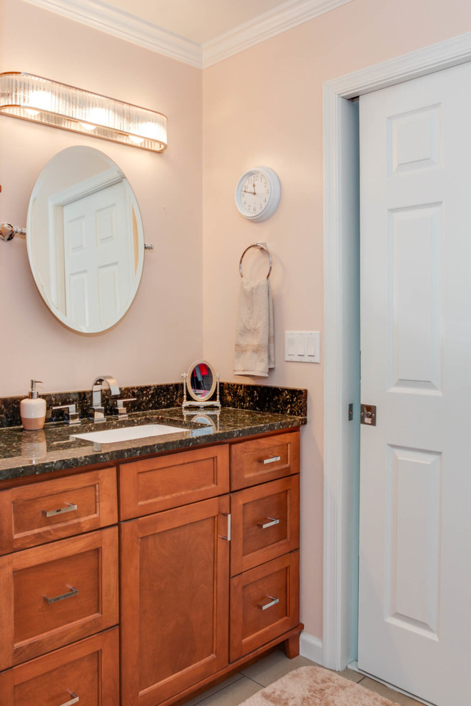 Cette image montre une salle de bain principale traditionnelle de taille moyenne avec un placard à porte shaker, des portes de placard marrons, une baignoire posée, un combiné douche/baignoire, WC à poser, un carrelage gris, un carrelage métro, un mur beige, un sol en carrelage de céramique, un lavabo encastré et un plan de toilette en granite.