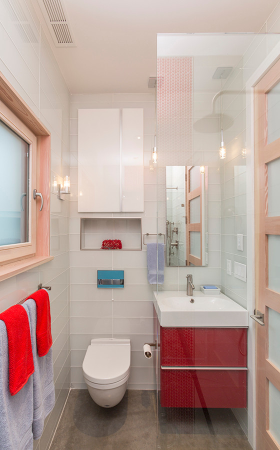 Modern inredning av ett litet en-suite badrum, med släta luckor, röda skåp, vit kakel, glaskakel, bänkskiva i akrylsten, en vägghängd toalettstol, vita väggar, betonggolv, ett nedsänkt handfat, grått golv, med dusch som är öppen och en dusch i en alkov
