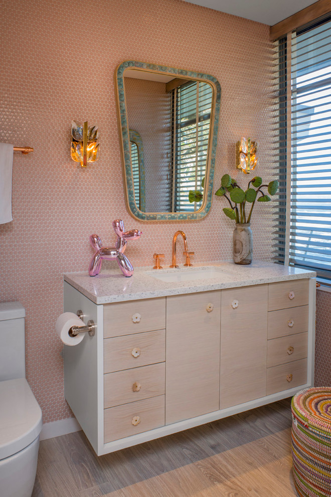 Cette photo montre une salle de bain rétro en bois clair avec un placard à porte plane, un carrelage rose, mosaïque, un lavabo encastré, un sol marron et un plan de toilette blanc.