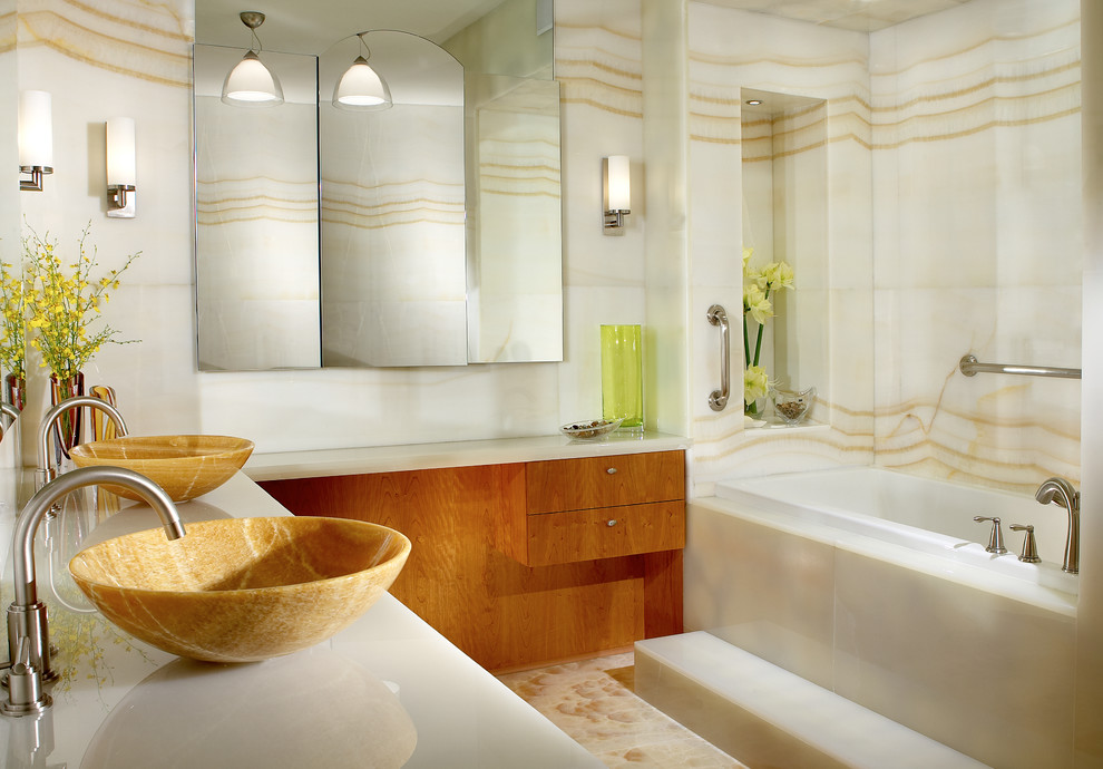 マイアミにあるラグジュアリーな広いコンテンポラリースタイルのおしゃれなマスターバスルーム (ベッセル式洗面器、オープンシェルフ、中間色木目調キャビネット、オニキスの洗面台、ドロップイン型浴槽、ダブルシャワー、一体型トイレ	、白いタイル、ガラスタイル、白い壁、大理石の床) の写真