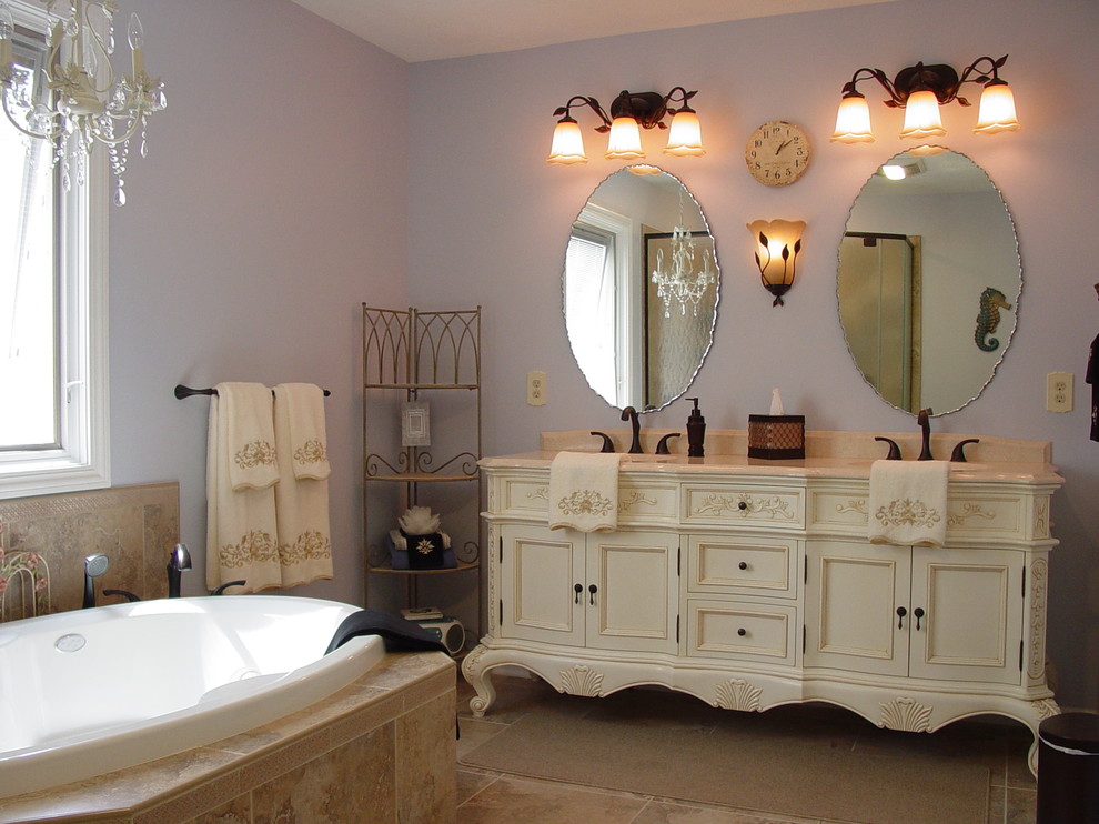 Diseño de cuarto de baño principal romántico grande con armarios con rebordes decorativos, puertas de armario beige, bañera encastrada, paredes púrpuras, suelo de travertino, lavabo bajoencimera, encimera de mármol y suelo marrón