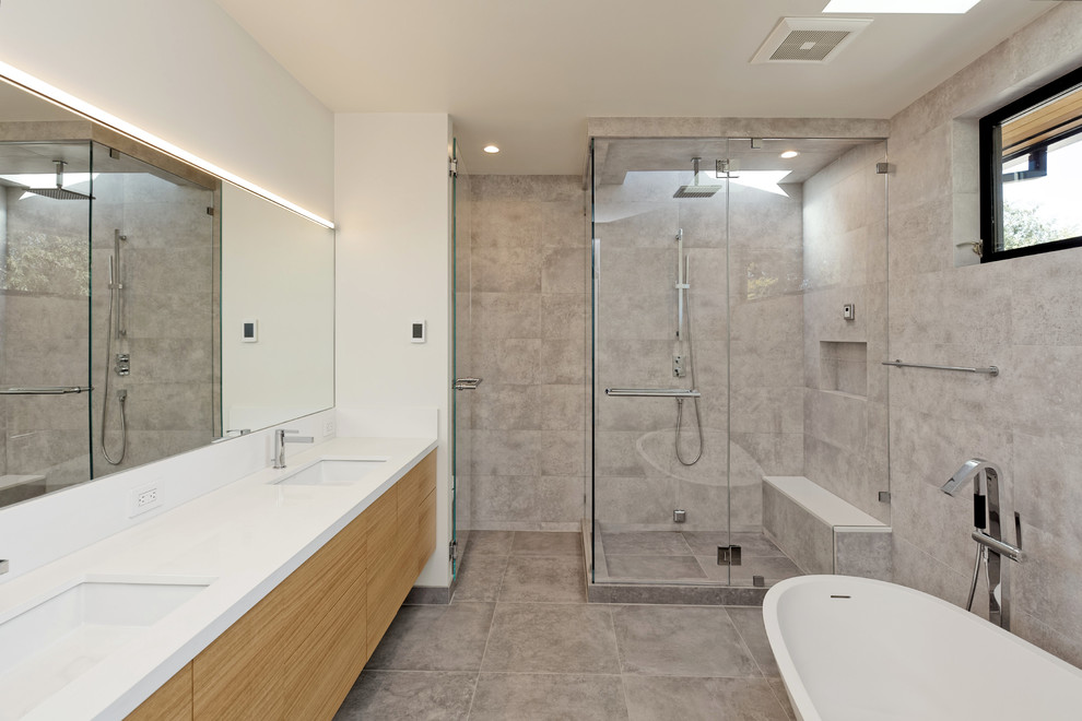 Свежая идея для дизайна: главная ванная комната среднего размера в современном стиле с плоскими фасадами, светлыми деревянными фасадами, отдельно стоящей ванной, угловым душем, инсталляцией, серой плиткой, керамогранитной плиткой, серыми стенами, бетонным полом, врезной раковиной, столешницей из искусственного камня, серым полом, душем с распашными дверями и белой столешницей - отличное фото интерьера