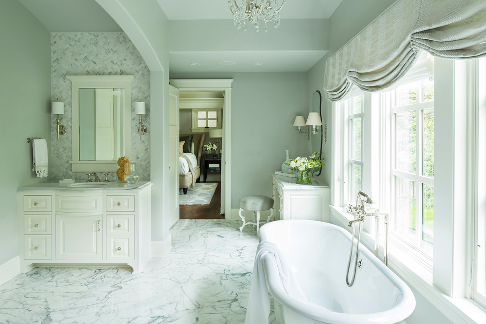 Klassisk inredning av ett badrum, med ett undermonterad handfat, luckor med upphöjd panel, vita skåp, marmorbänkskiva, grå kakel och stenkakel
