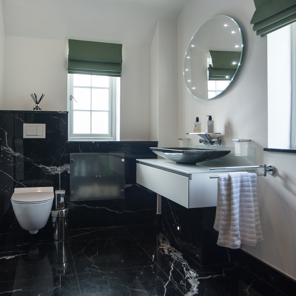 Inspiration för stora moderna badrum, med en vägghängd toalettstol, svart och vit kakel, marmorgolv, bänkskiva i glas, släta luckor, vita skåp, vita väggar och ett fristående handfat