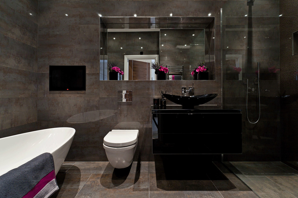 На фото: ванная комната в современном стиле с настольной раковиной, плоскими фасадами, черными фасадами, отдельно стоящей ванной, инсталляцией и коричневой плиткой с