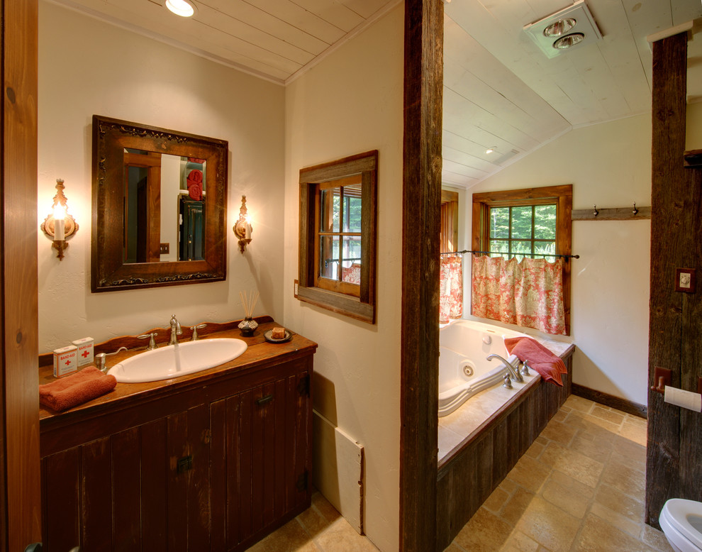 Cette image montre une douche en alcôve chalet de taille moyenne avec un lavabo posé, un plan de toilette en bois, un bain bouillonnant, WC séparés, un carrelage beige, un carrelage de pierre, un mur beige et un sol en travertin.