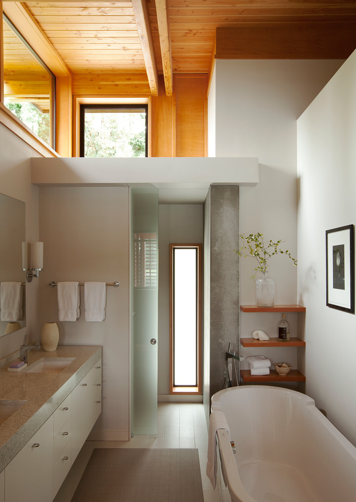 Modern inredning av ett en-suite badrum, med ett undermonterad handfat, släta luckor, vita skåp, ett fristående badkar, en kantlös dusch, vita väggar och klinkergolv i keramik