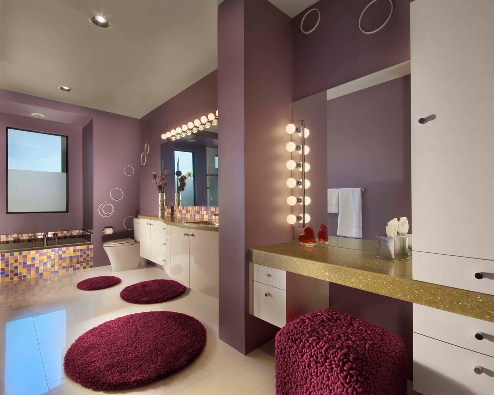 Cette image montre une salle de bain design pour enfant avec un placard à porte plane, un plan de toilette en quartz, une baignoire en alcôve, WC à poser, un carrelage multicolore, mosaïque, des portes de placard blanches, un mur violet, un sol en carrelage de porcelaine et une fenêtre.
