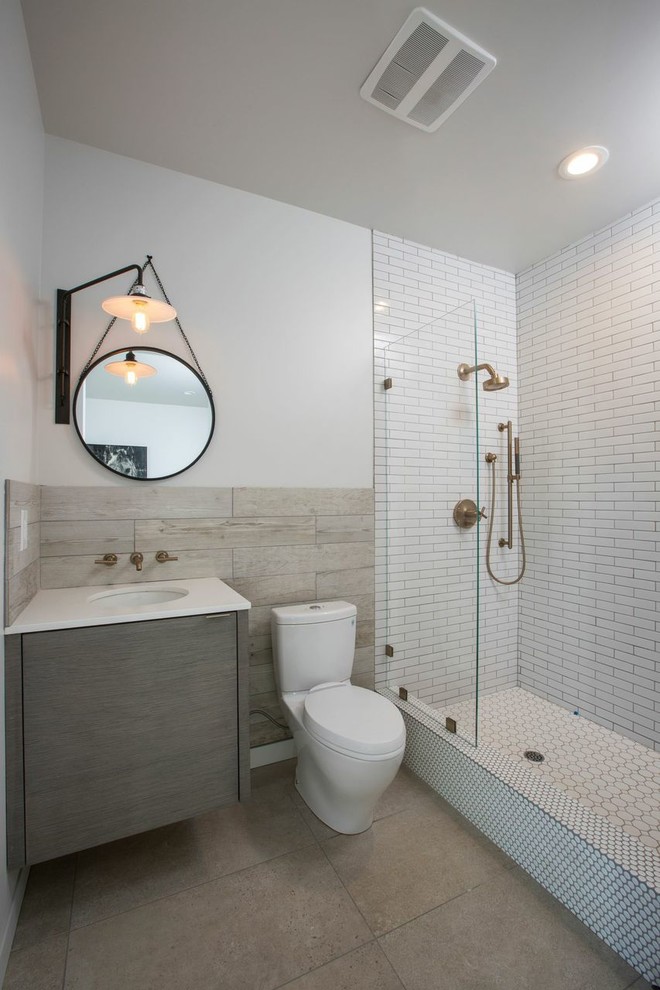 Modern inredning av ett badrum, med ett undermonterad handfat, släta luckor, grå skåp, en dusch i en alkov, en toalettstol med separat cisternkåpa, vit kakel, tunnelbanekakel och vita väggar