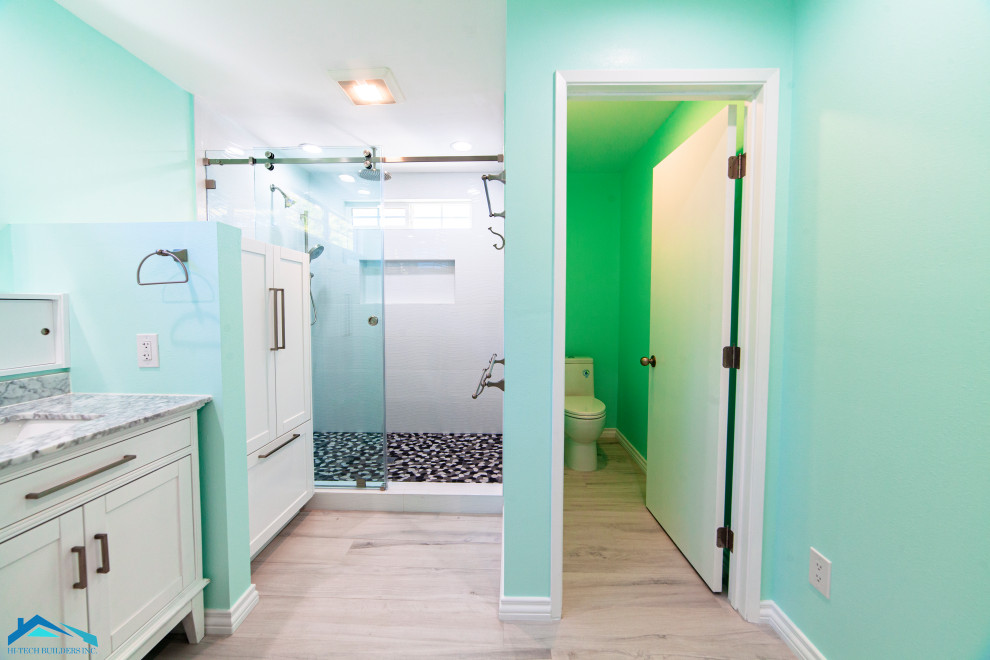 Foto på ett stort funkis badrum med dusch, med skåp i shakerstil, vita skåp, en dusch i en alkov, en toalettstol med hel cisternkåpa, vit kakel, gröna väggar, laminatgolv, ett undermonterad handfat, granitbänkskiva, beiget golv och dusch med skjutdörr