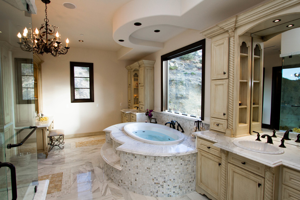 Inredning av ett medelhavsstil stort en-suite badrum, med luckor med upphöjd panel, beige skåp, ett platsbyggt badkar, en hörndusch, beige kakel, grå kakel, vit kakel, mosaik, beige väggar, marmorgolv, ett nedsänkt handfat och marmorbänkskiva
