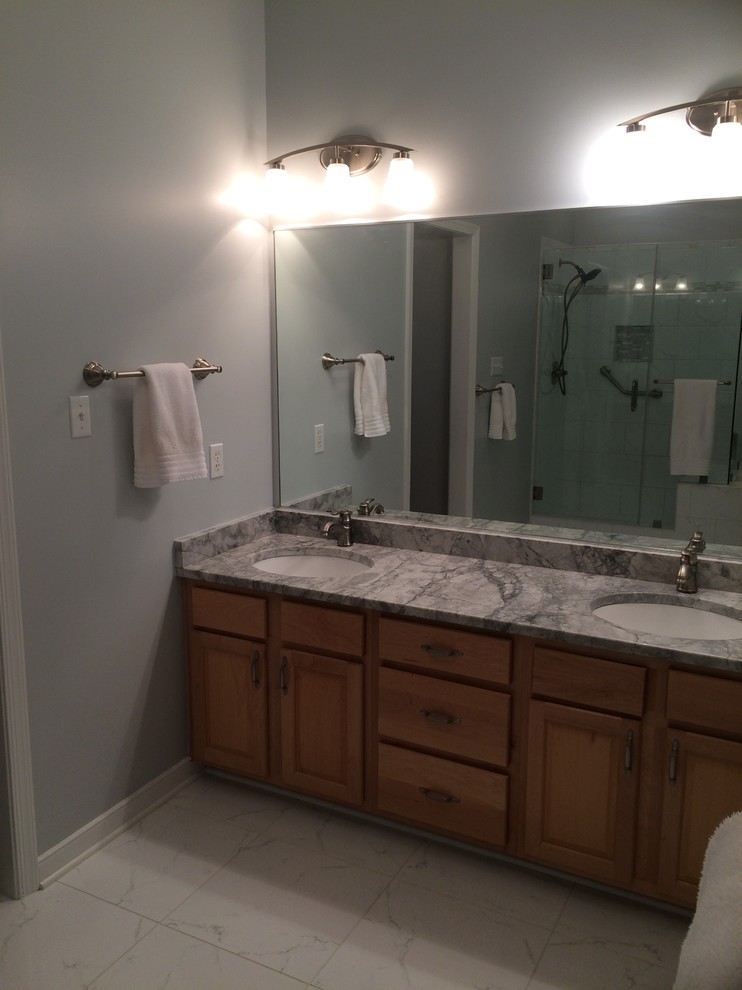 Inredning av ett klassiskt badrum, med ett hörnbadkar, vit kakel, porslinskakel, grå väggar, klinkergolv i porslin, ett undermonterad handfat och granitbänkskiva