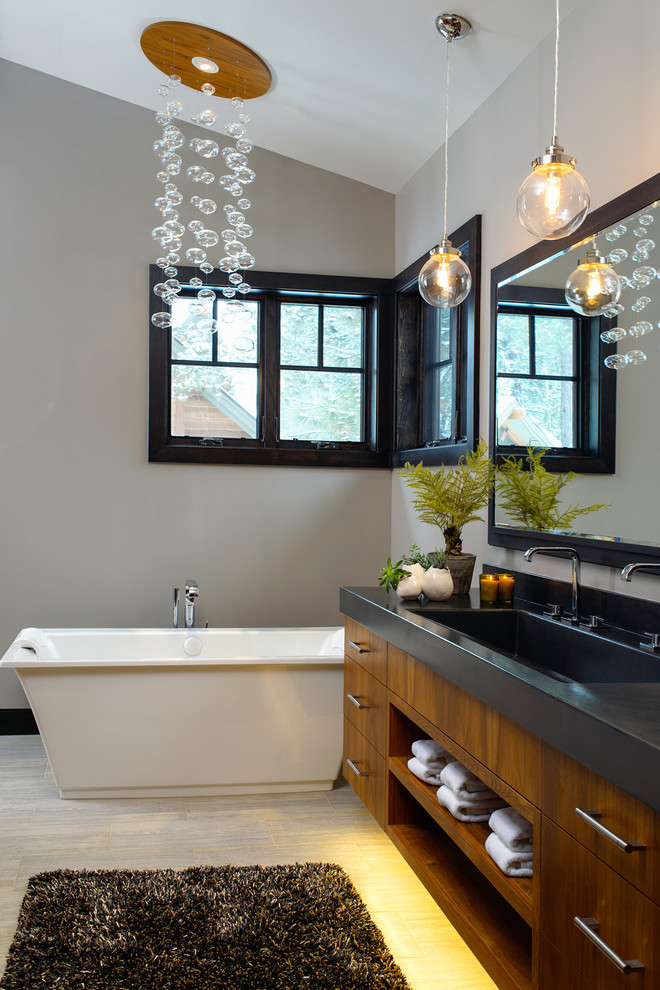 На фото: ванная комната в современном стиле с раковиной с несколькими смесителями, открытыми фасадами, темными деревянными фасадами, столешницей из бетона, отдельно стоящей ванной и серыми стенами