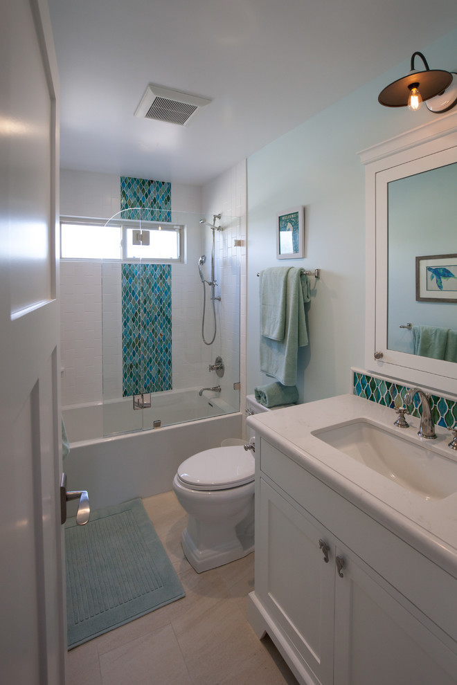 Photo of a small coastal family bathroom in Los Angeles with a submerged sink, recessed-panel cabinets, white cabinets, solid surface worktops, an alcove shower, a two-piece toilet, white tiles, metro tiles, blue walls and porcelain flooring.