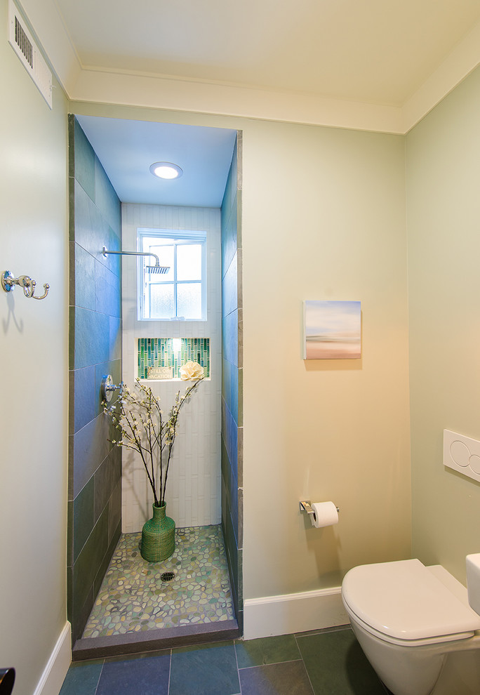 Bild på ett maritimt badrum med dusch, med en dusch i en alkov, en vägghängd toalettstol, flerfärgad kakel, vita väggar och skiffergolv