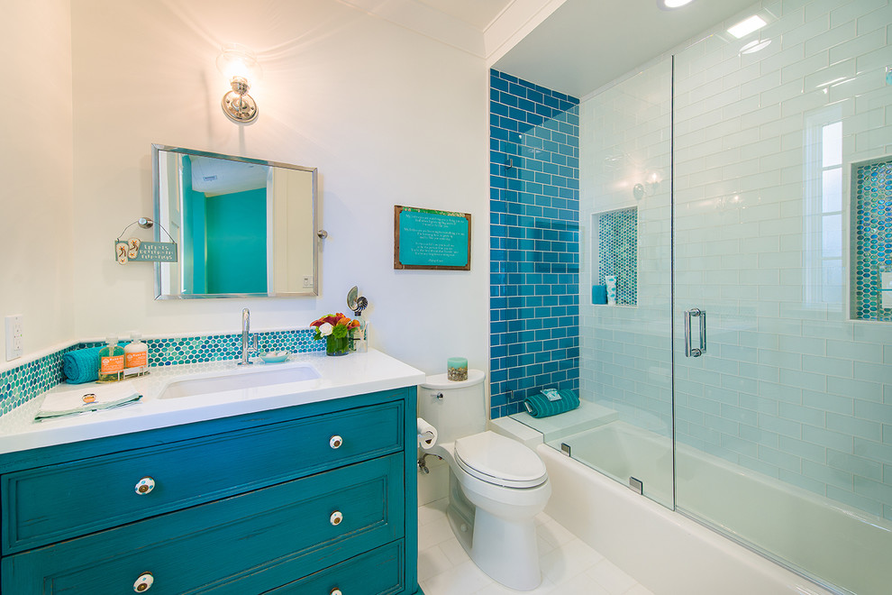 Design ideas for a medium sized coastal shower room bathroom in Los Angeles with a built-in sink, recessed-panel cabinets, blue cabinets, engineered stone worktops, an alcove bath, a shower/bath combination, a one-piece toilet, blue tiles, mosaic tiles, white walls, ceramic flooring, white floors, a hinged door and white worktops.