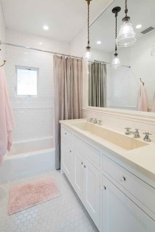 Inspiration for a coastal bathroom in Santa Barbara with white cabinets, a shower/bath combination, white tiles, metro tiles, white walls, porcelain flooring, white floors, a shower curtain, beige worktops, double sinks, a built in vanity unit, shaker cabinets, a trough sink and an alcove bath.