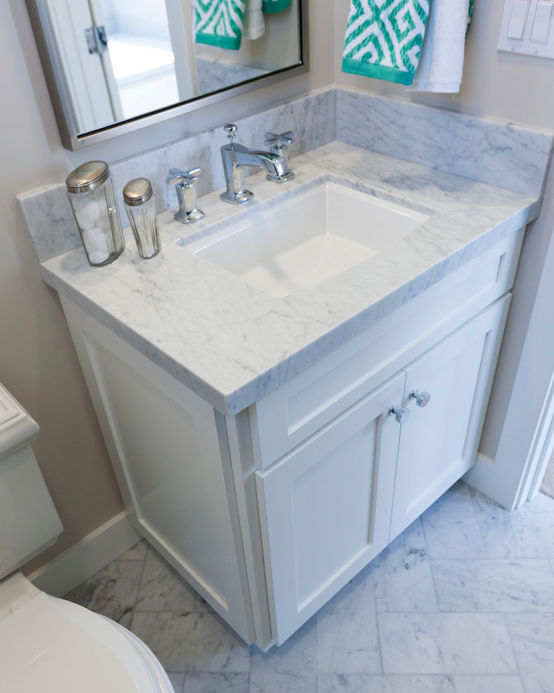 Maritim inredning av ett badrum med dusch, med ett undermonterad handfat, skåp i shakerstil, vita skåp, marmorbänkskiva, en dusch i en alkov, en toalettstol med separat cisternkåpa, grå kakel, stenkakel, grå väggar och marmorgolv
