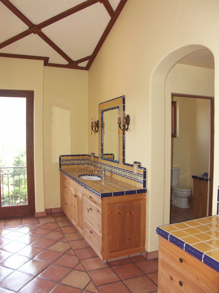 Idées déco pour une salle de bain principale méditerranéenne en bois clair avec un lavabo encastré, un placard à porte shaker, un plan de toilette en carrelage, un carrelage jaune, des carreaux de céramique, un mur jaune et tomettes au sol.