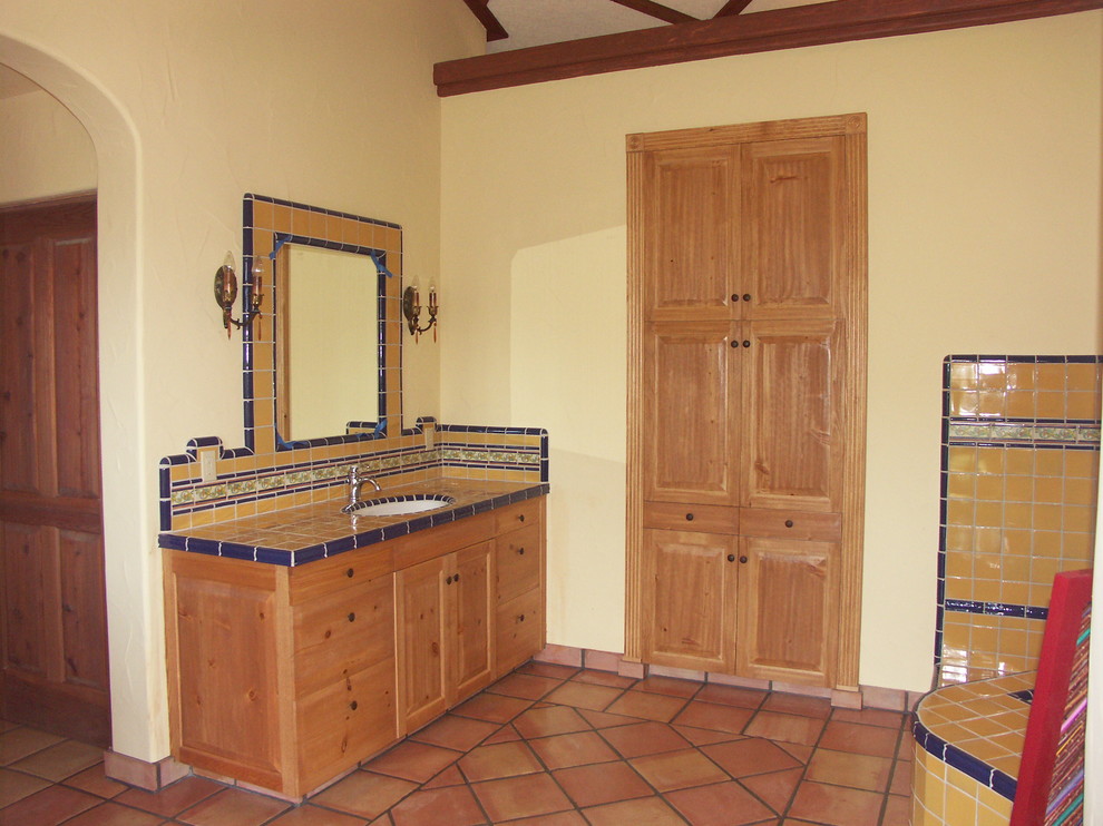 Cette image montre une salle de bain principale méditerranéenne en bois clair avec un lavabo encastré, un placard à porte shaker, une baignoire d'angle, un carrelage jaune, des carreaux de céramique, un mur jaune et tomettes au sol.