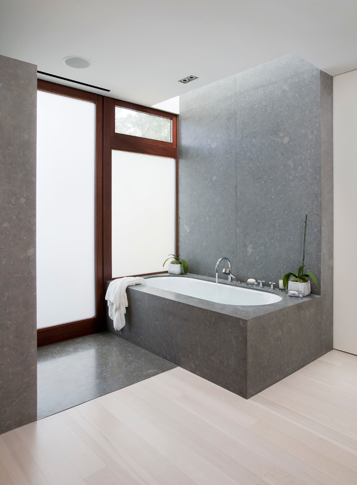 Cette image montre une salle de bain design avec une baignoire encastrée, un mur gris et parquet clair.