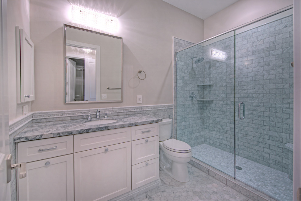 Esempio di una stanza da bagno con doccia costiera di medie dimensioni con ante in stile shaker, ante bianche, doccia alcova, WC a due pezzi, piastrelle grigie, piastrelle bianche, piastrelle in pietra, pareti beige, pavimento in marmo, lavabo sottopiano e top in marmo