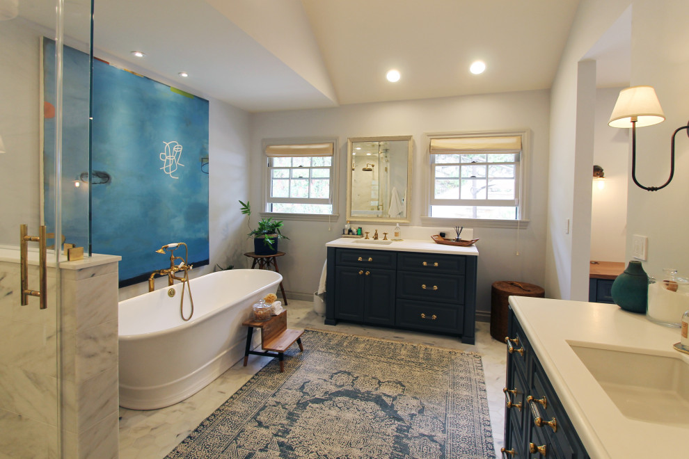 This is an example of an expansive traditional ensuite bathroom in Los Angeles with raised-panel cabinets, blue cabinets, a freestanding bath, an alcove shower, a two-piece toilet, white tiles, porcelain tiles, white walls, marble flooring, a submerged sink, concrete worktops, white floors, a hinged door, grey worktops, a wall niche, a single sink, a built in vanity unit, a vaulted ceiling and tongue and groove walls.