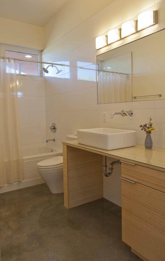 Ispirazione per una stanza da bagno minimalista con lavabo a bacinella, ante lisce, ante in legno chiaro, vasca ad alcova, vasca/doccia, WC a due pezzi, piastrelle bianche e pavimento in cemento