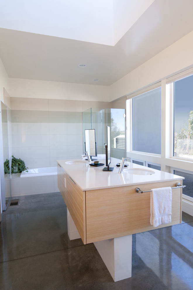 Foto de cuarto de baño moderno con armarios con paneles lisos, puertas de armario de madera clara, suelo de cemento, bañera encastrada y encimeras blancas