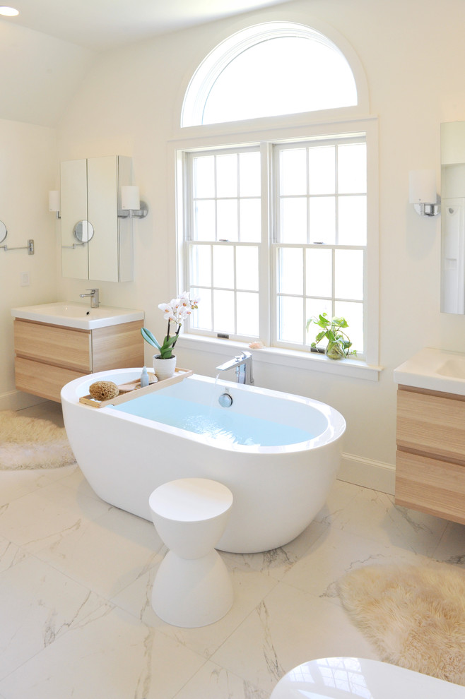 Mid-sized trendy master white tile and ceramic tile marble floor freestanding bathtub photo in Providence with light wood cabinets, white walls, an integrated sink, flat-panel cabinets and a one-piece toilet