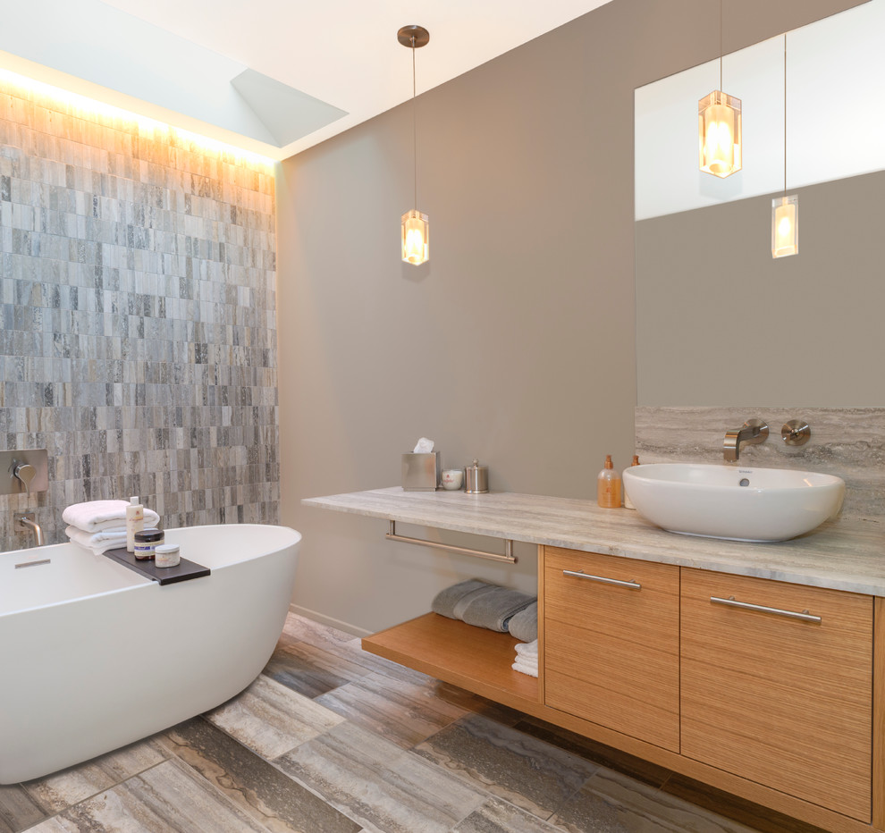 Réalisation d'une salle de bain principale design en bois brun avec une vasque, un placard à porte plane, un plan de toilette en marbre, une baignoire indépendante, un carrelage gris, un carrelage de pierre et un mur gris.