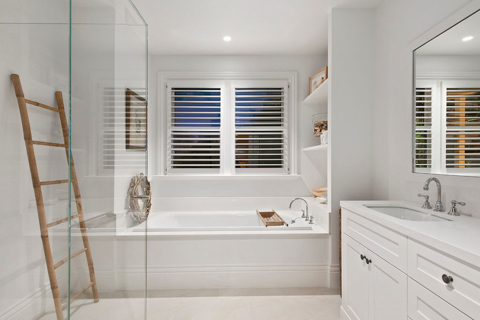 Diseño de cuarto de baño costero con armarios estilo shaker, puertas de armario blancas, bañera encastrada, baldosas y/o azulejos blancos, paredes blancas y lavabo bajoencimera