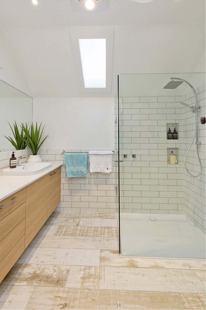 Inredning av ett modernt mellanstort badrum, med släta luckor, skåp i ljust trä, vit kakel, vita väggar, bänkskiva i kvarts, en kantlös dusch, tunnelbanekakel och ett nedsänkt handfat