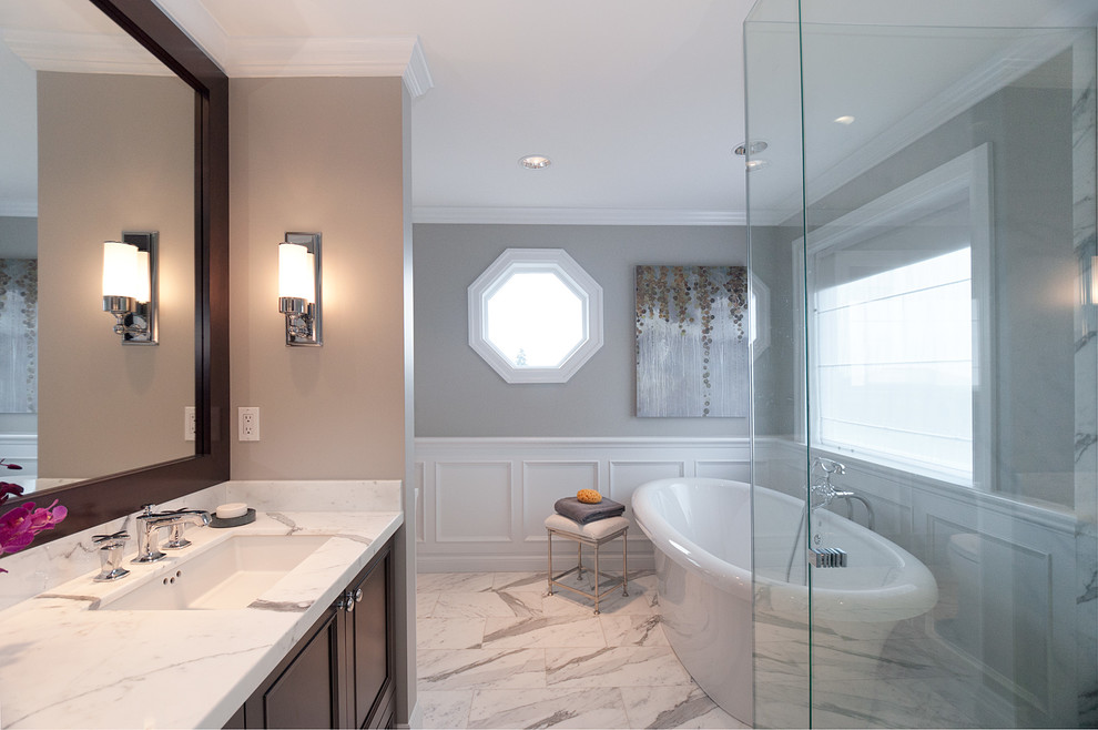 Aménagement d'une salle de bain classique en bois foncé avec un lavabo encastré, un placard avec porte à panneau encastré, un plan de toilette en marbre et une baignoire indépendante.