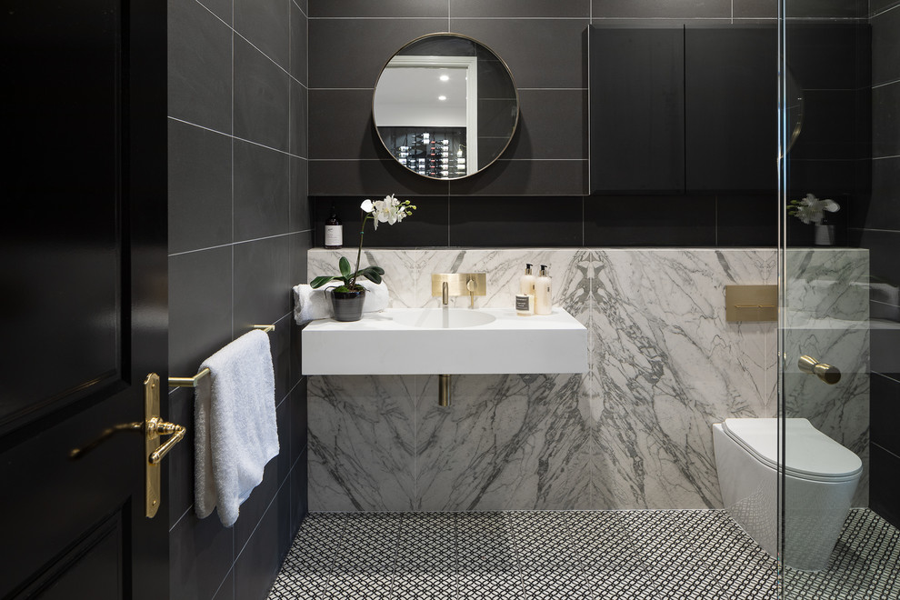 Modern inredning av ett vit vitt badrum med dusch, med en hörndusch, en toalettstol med hel cisternkåpa, svart kakel, grå kakel, ett väggmonterat handfat, flerfärgat golv och dusch med gångjärnsdörr