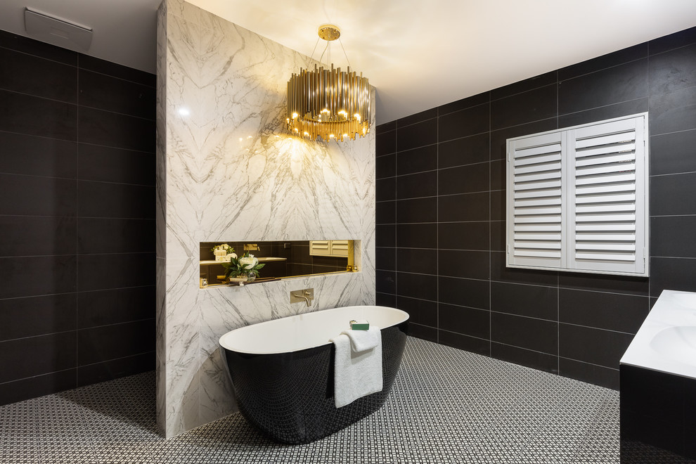Cette image montre une salle de bain design avec des portes de placard noires, une baignoire indépendante, un espace douche bain, un carrelage noir, un lavabo intégré, un sol multicolore, aucune cabine, un plan de toilette blanc et du carrelage bicolore.